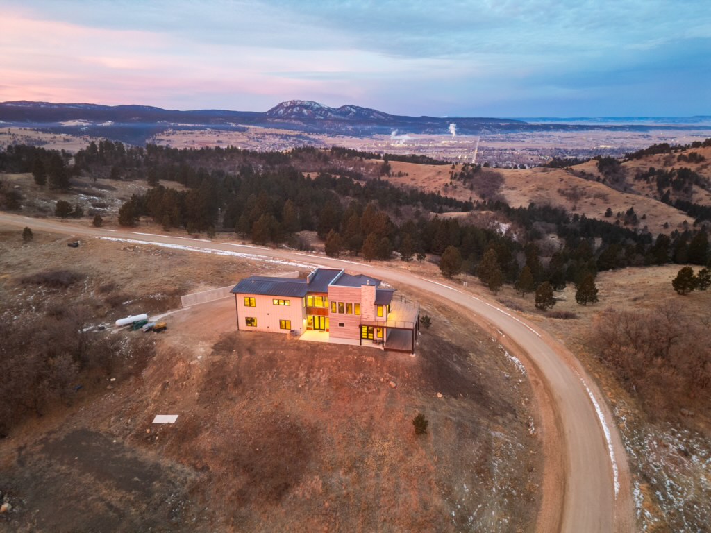 At dusk, an aerial view shows the home's curving gravel driveway meeting the road, with the valley and mountains beyond.