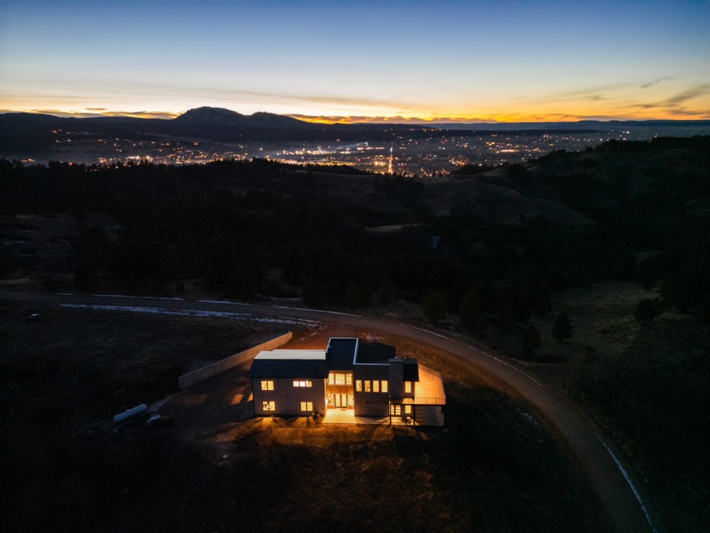 Another night aerial view captures the lit house with the scattered lights of the valley visible in the distance.