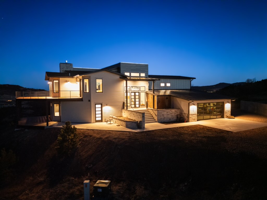 A three-quarter night view shows the lit house from the driveway side