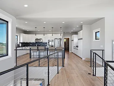A hallway with cable railing leads toward the kitchen and pendant lights at 2111 Vantage Circle.
