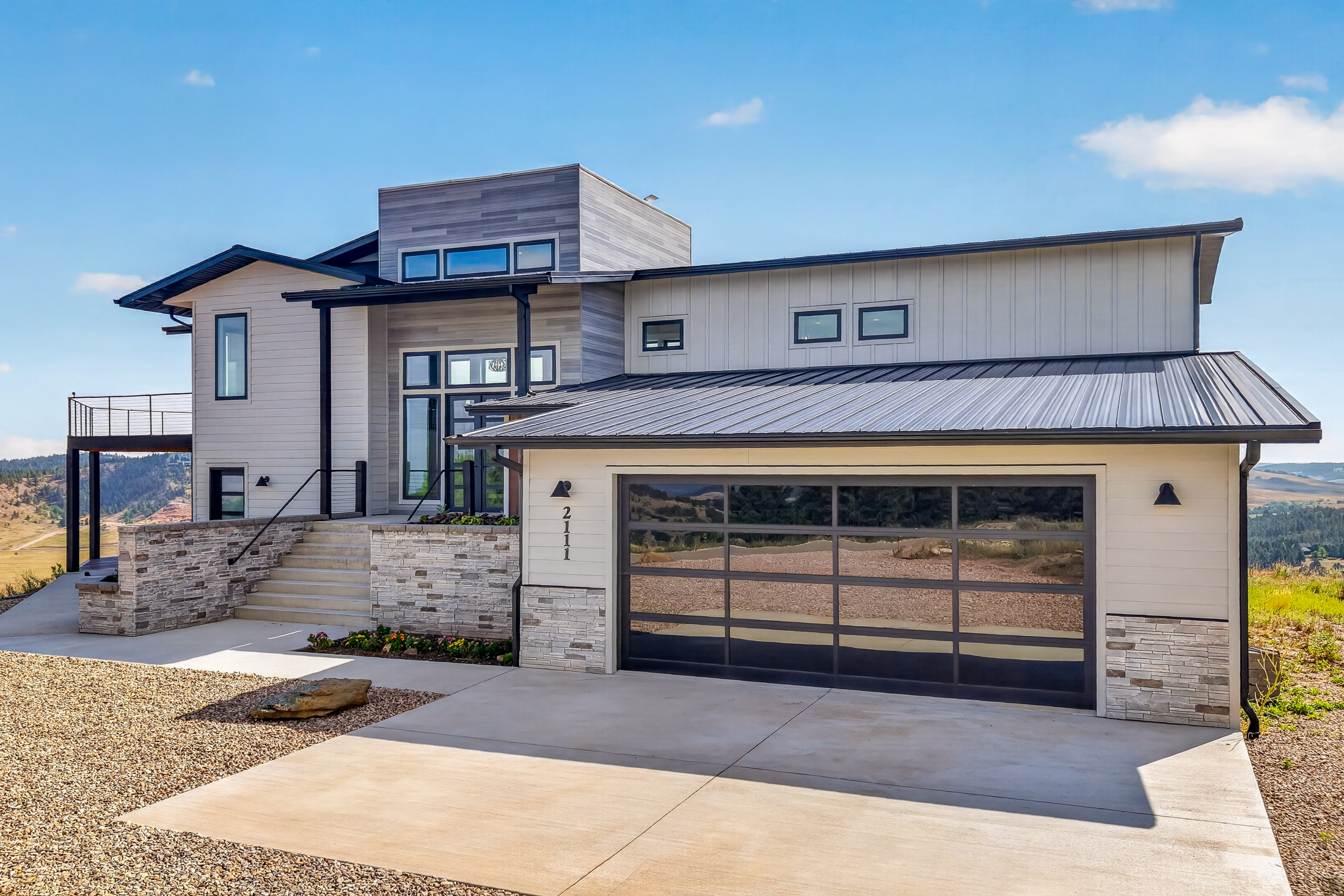 The front of the home shows a glass-panel garage door, stacked stone accents, and the address number 2111 mounted beside the entry stairs.