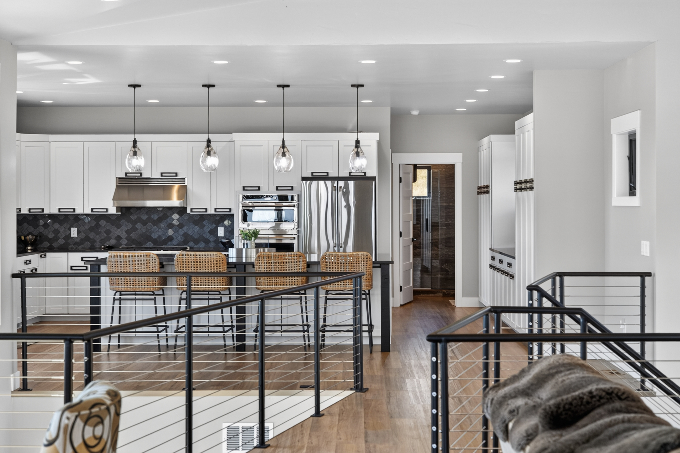 Four glass pendant lights hang over the kitchen island at 2111 Vantage Circle, with woven barstools and a stainless refrigerator beyond.