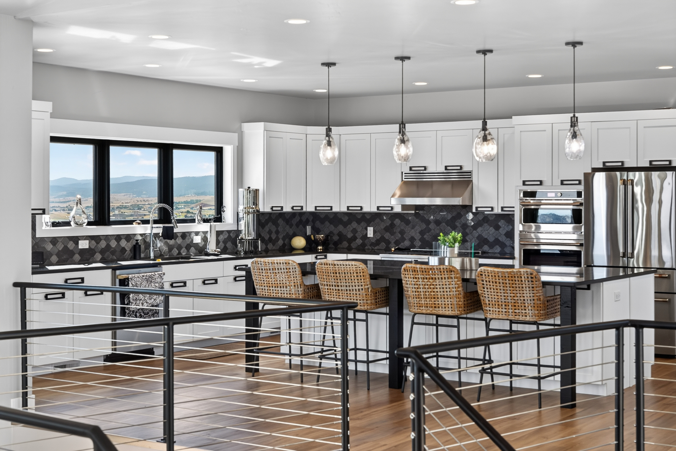 The kitchen's sink and gas range sit along a dark tile backsplash, with a three-panel window looking out over distant mountains.