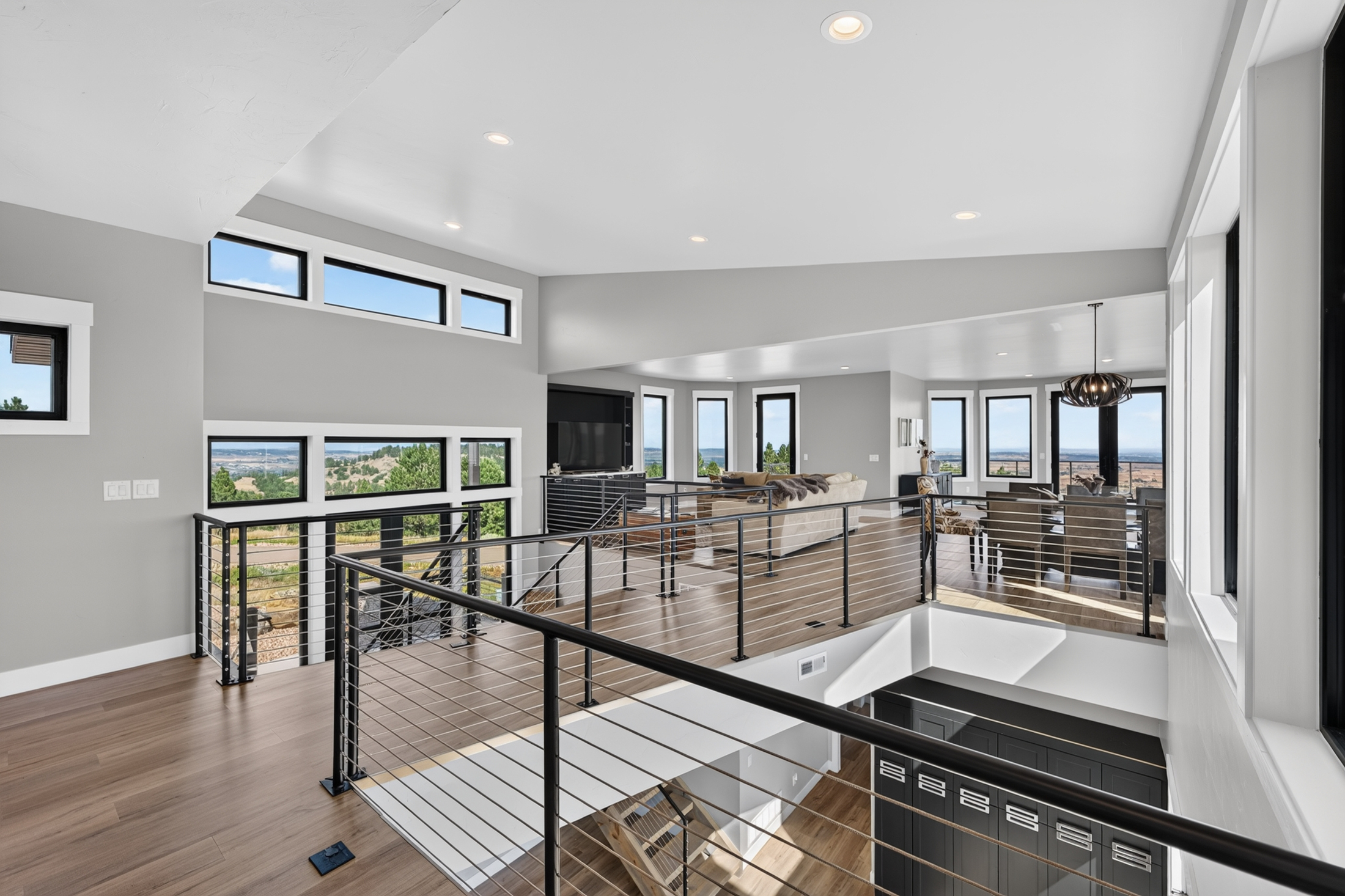 A loft landing with black cable railing looks down over the great room