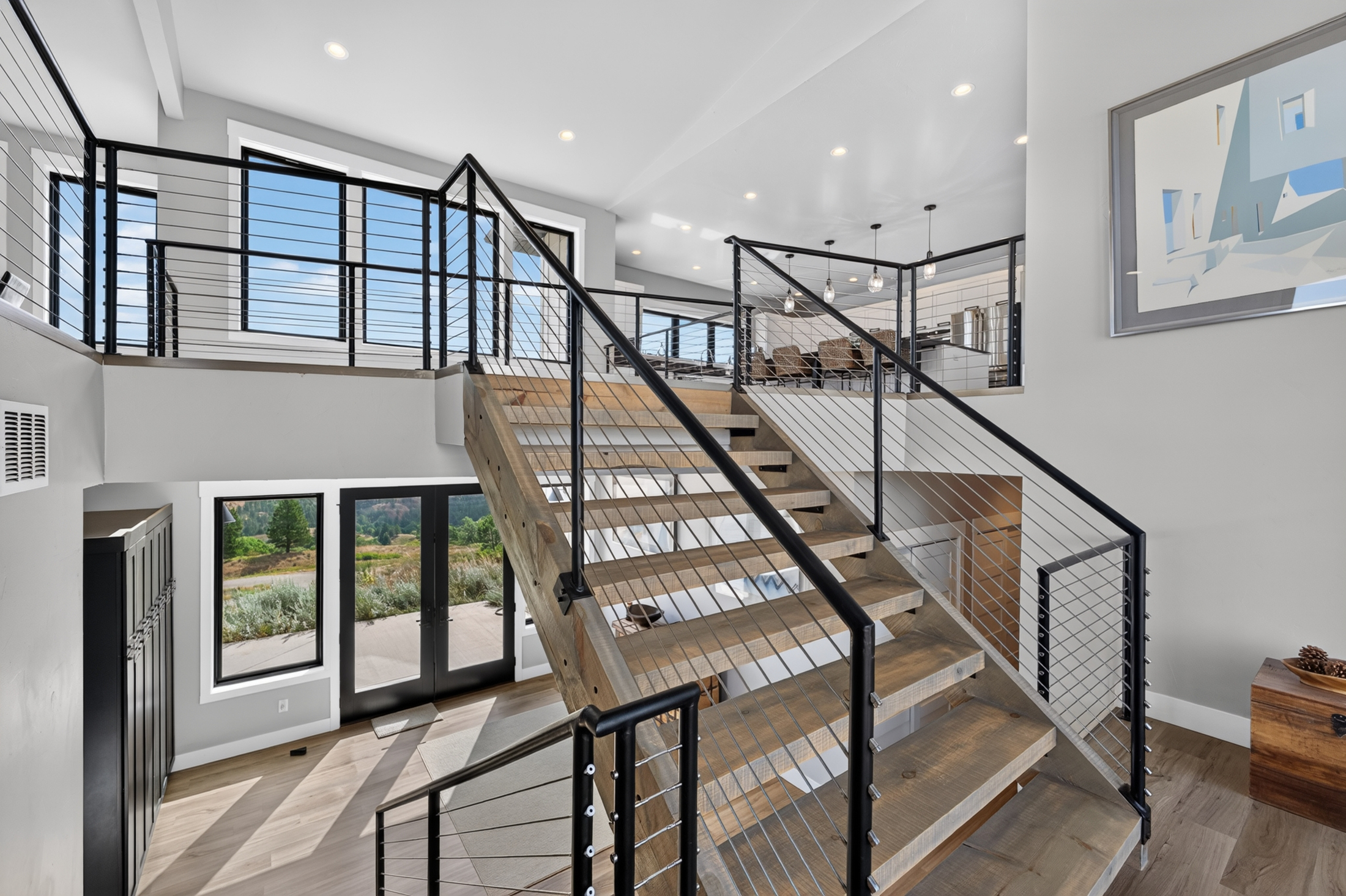 Cable railings line the stairway landing at 2111 Vantage Circle, with an abstract painting on the wall and glass doors opening to the deck.
