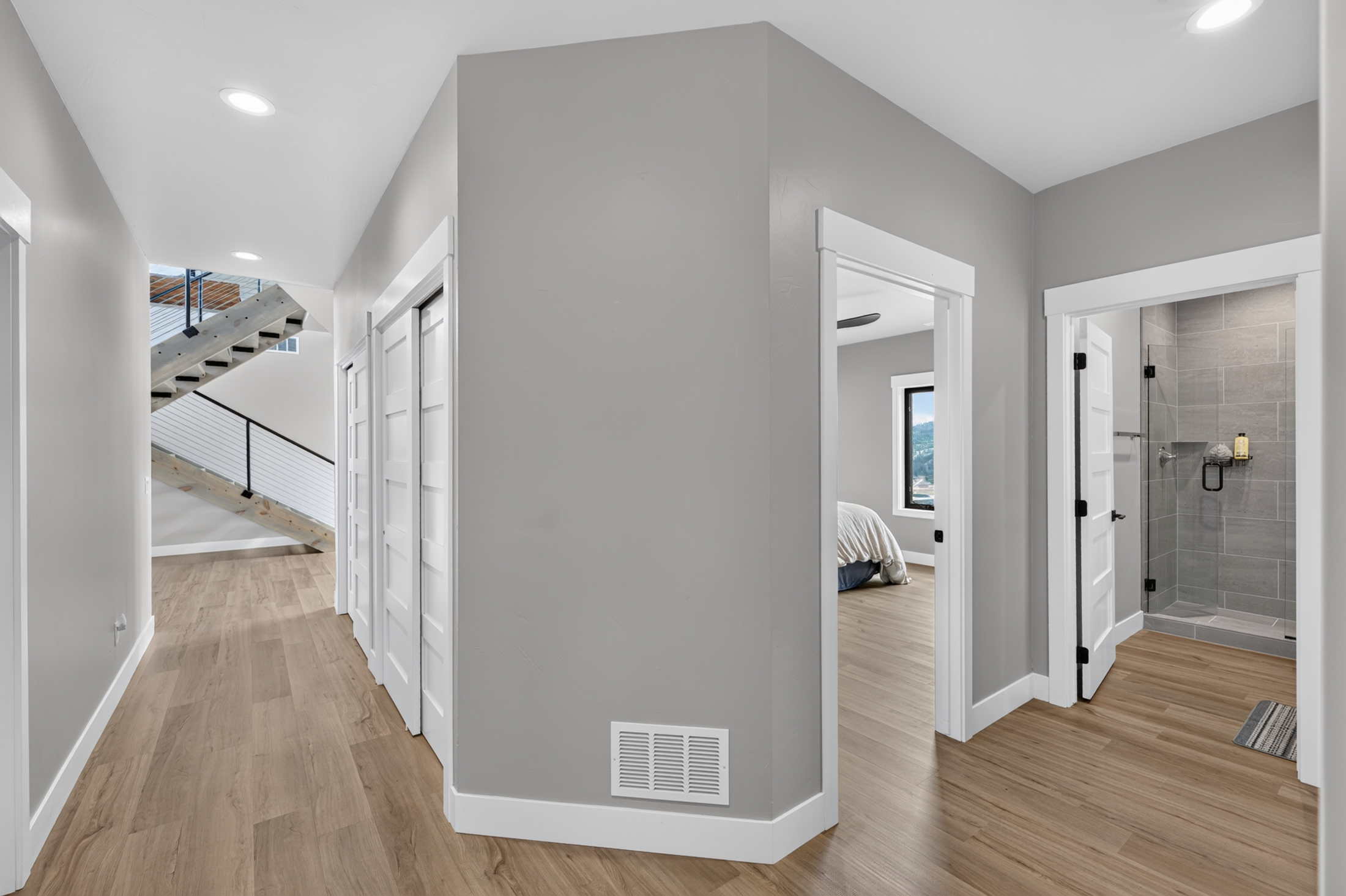 An upstairs hallway with an open staircase leads past a bedroom doorway to a tiled walk-in shower at 2111 Vantage Circle.